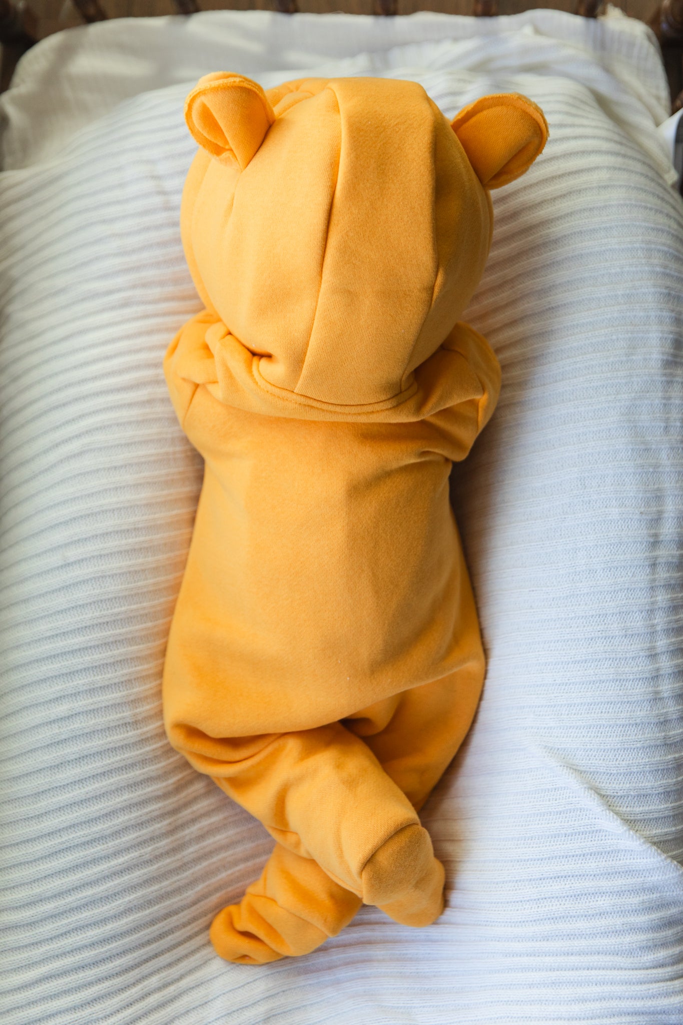 Baby in a yellow bear onesie lying on a white blanket