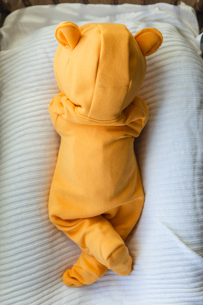 Baby in a yellow bear onesie lying on a white blanket