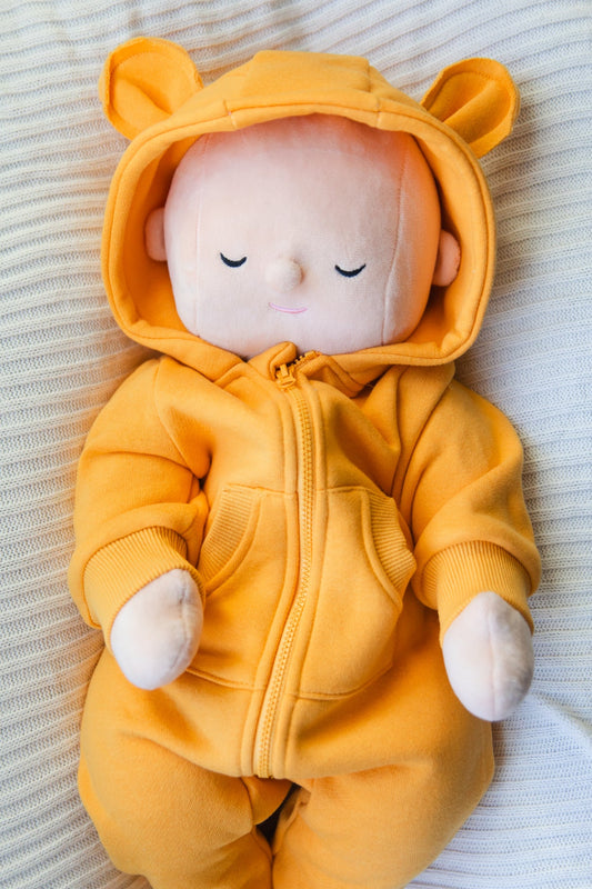 Baby doll wearing a yellow onesie with bear ears on a soft surface